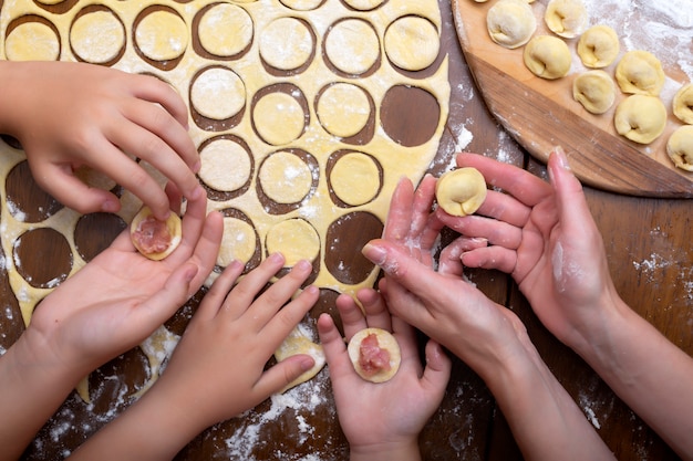 Cuisinez des raviolis de pâte et de viande avec toute la famille. Mains des femmes et des enfants. Raviolis faits maison.