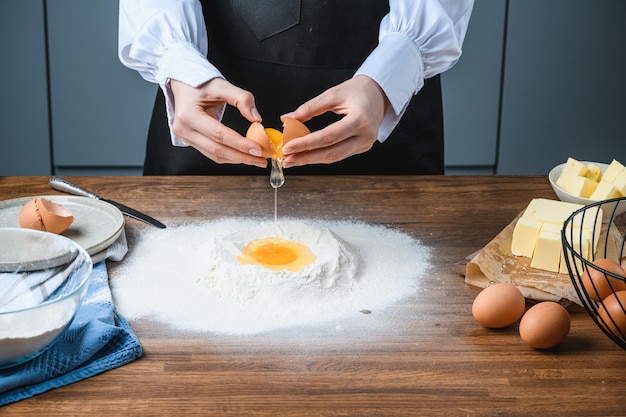 Le cuisinier casse un œuf en farine de cuisson sur la table avec les ingrédients.