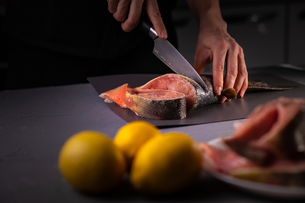 cuisinier coupe le poisson en morceaux avec un couteau sur une planche grise