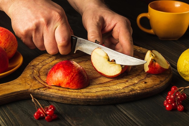 Le cuisinier coupe les pommes sur une planche à découper avec un couteau pour faire de la compote ou du jus de fruits pour le régime Apple