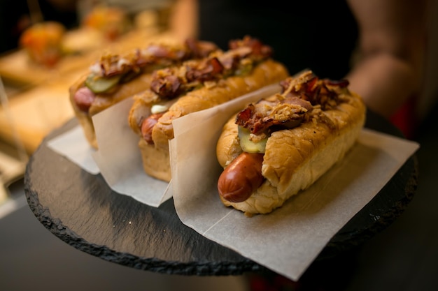 cuisinier dans des gants noirs tient un hot-dog Le cuisinier prépare un hot-dog en ajoutant la sauce à la saucisse