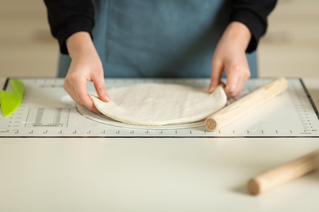 Un cuisinier dans un tablier bleu prend la pâte déroulée d'un tapis de cuisson en silicone de cuisine Vue des mains et de l'espace de copie de l'espace de travail