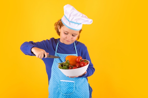 Cuisinier enfant tenant une assiette avec des légumes Chef cuisinier enfant prépare la nourriture sur fond de studio isolé