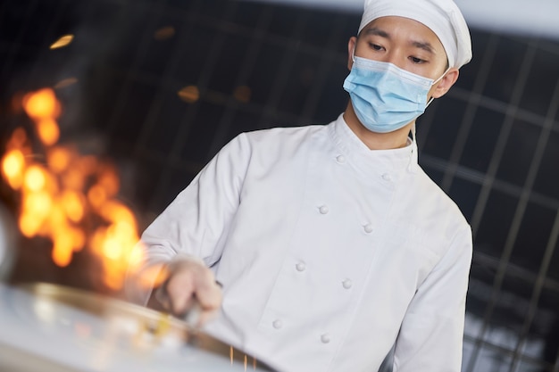 Cuisinier expérimenté faisant des sautés avec des flammes dans un wok