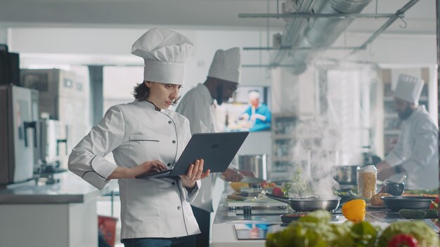 Cuisinier féminin regardant l'écran d'ordinateur portable pour suivre la recette de nourriture