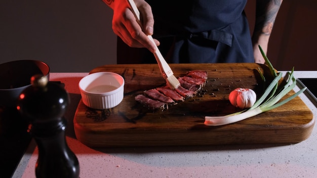 Photo le cuisinier graisse les tranches de viande avec de l'huile d'olive avant de les servir