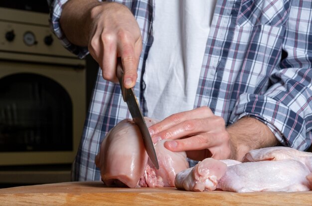 Un cuisinier masculin coupe du poulet frais fait maison sur une planche de bois