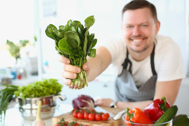 Cuisinier masculin souriant tenant de l'oseille ou de la salade dans la cuisine