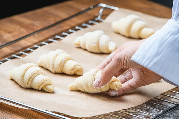 Le cuisinier met des croissants sur une plaque à pâtisserie sur la table avec des ingrédients