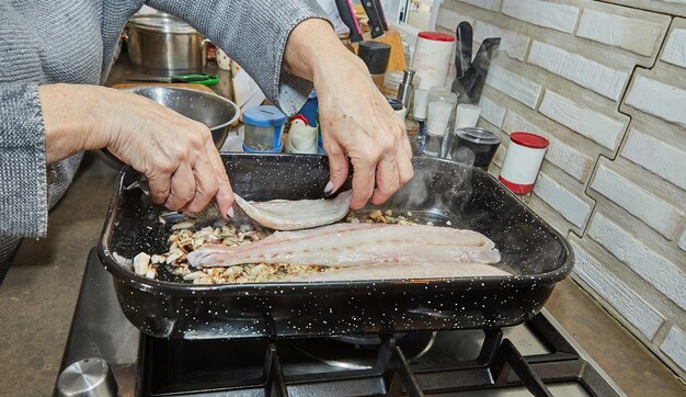 Le cuisinier met du poisson sur des champignons avec des oignons dans une casserole carrée sur une cuisinière à gaz