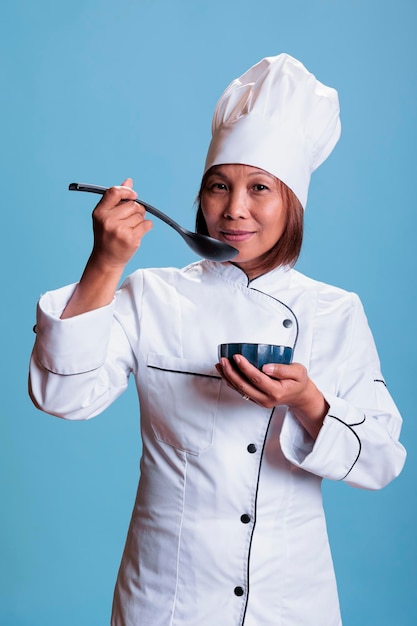 Cuisinier positif confiant tenant un bol de cuisine dégustant un repas préparé en studio avec un fond bleu. Chef gai cuisinant un plat de dîner à l'aide d'ingrédients sains, industrie de la gastronomie