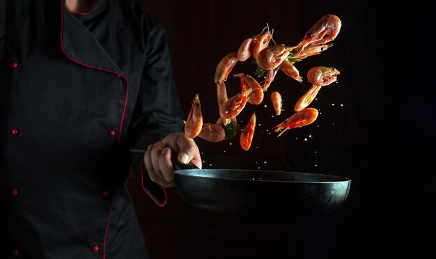 Photo le cuisinier prépare des crevettes dans une poêle à frire avec du persil le concept de cuisiner des fruits de mer et des aliments végétariens sains sur un fond sombre