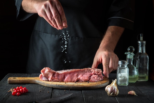 Le cuisinier prépare la viande de veau crue Avant la cuisson, le chef ajoute du sel au boeuf