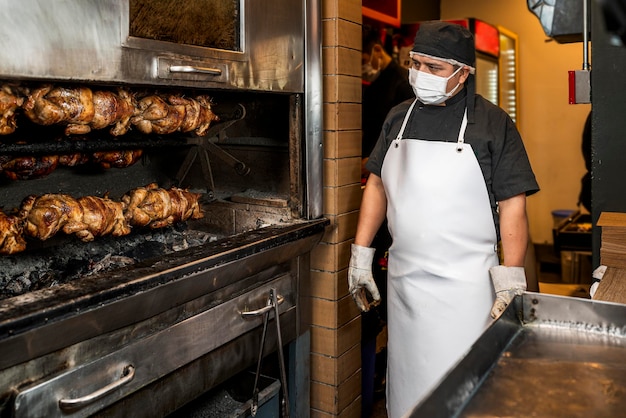 Cuisinier professionnel regardant une pile de poulet grillé sur une brochette dans le gril