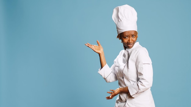 Cuisinier professionnel en tablier pointant vers la gauche ou la droite, créant une publicité de studio sur caméra. Joyeuse femme chef gastronomique montrant quelque chose de côté, travaillant dans l'industrie de la cuisine.