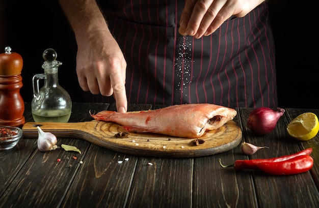 Le cuisinier saupoudre du poisson rouge ou du bar avec du sel Idée de menu ou délicieuse recette pour restaurant ou hôtel sur fond sombre