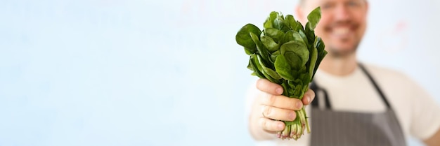 Un cuisinier souriant tient des feuilles de laitue ou d'oseille en gros plan