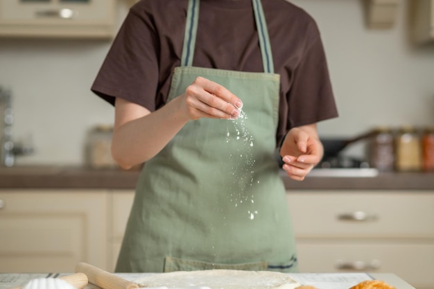 Un cuisinier en T-shirt marron et tablier vert cuisine avec de la farine dans la cuisine