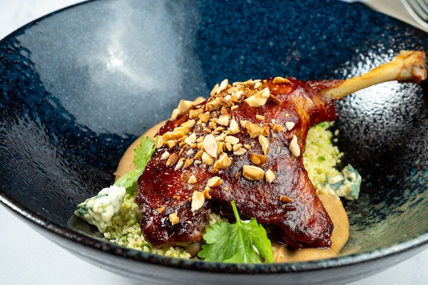 Cuisse de canard confite avec beurre d'arachide et fromage bleu dor dans un élégant bol sombre sur une table en marbre. Plat gourmand pour le déjeuner. Cuisine française.