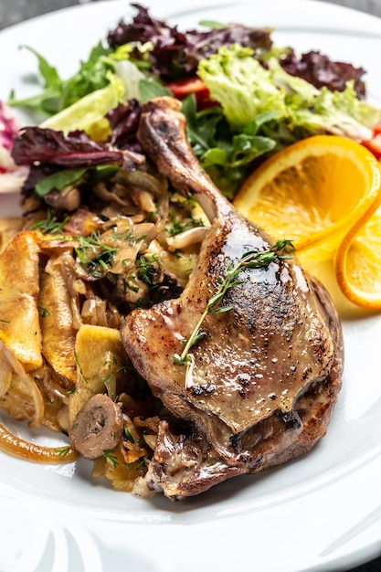 Cuisse de canard cuite délicieuse et juteuse servie avec des pommes de terre au four, des champignons et des oignons. Fond de recette de nourriture. Fermer.