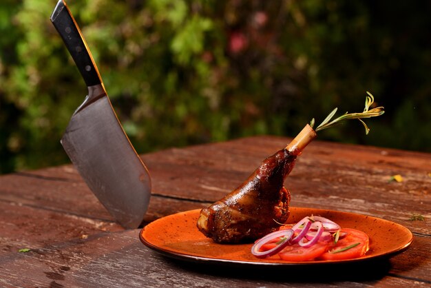 Cuisse de canard grillé aux légumes. Dans une assiette rouge sur une table en bois