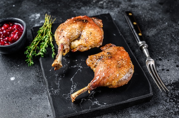 Cuisse de canard rôtie confite avec sauce aux canneberges. Fond noir. vue de dessus.