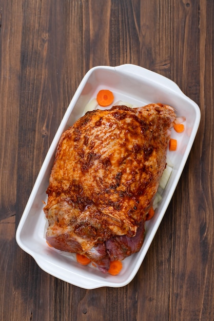 Cuisse de dinde crue aux épices et légumes sur un plat sur une surface en bois