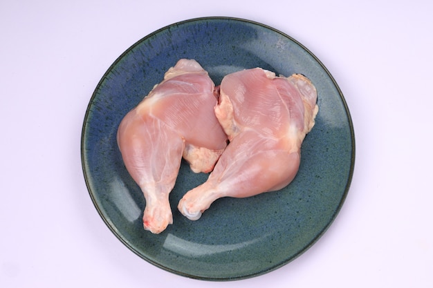 Cuisse de poulet entière crue sans peau disposée dans une assiette bleue rustique aqua avec fond blanc.