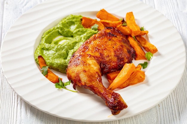 Photo cuisse de poulet frite avec sauce guasacaca de poivre vert avocat et herbes et chips de patate douce sur plaque blanche sur table en bois libre