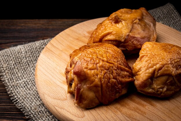 Cuisse de poulet fumé sur planche de bois sur fond de bois foncé.