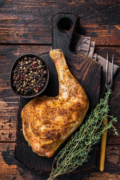 Cuisse de poulet grillée sur une planche de bois. Fond en bois sombre. Vue de dessus.