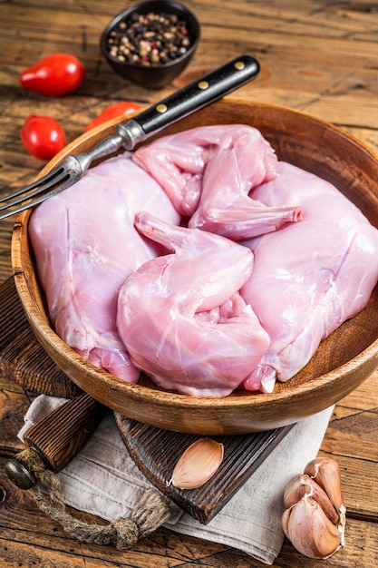 Cuisses de lapin non cuites dans une assiette en bois. Fond en bois. Vue de dessus.