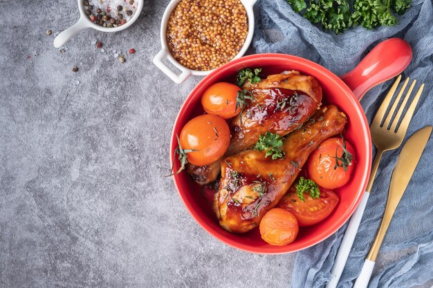 Cuisses de poulet au four dans une sauce barbecue avec des tomates dans une poêle à frire rouge