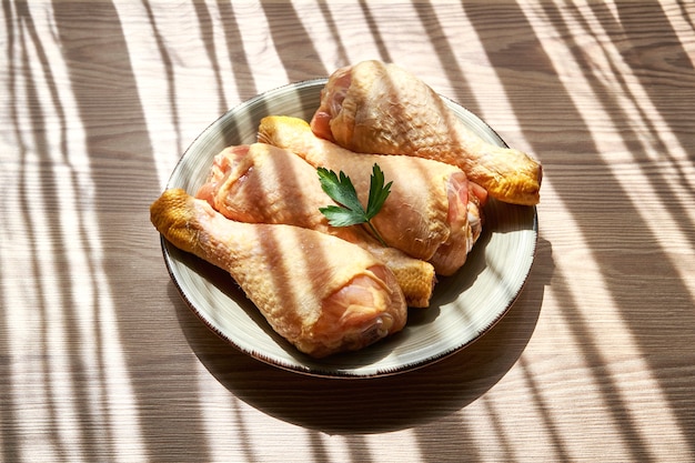 Cuisses de poulet crues sur une assiette sur une table en bois à côté d'une fenêtre qui laisse entrer les rayons du soleil