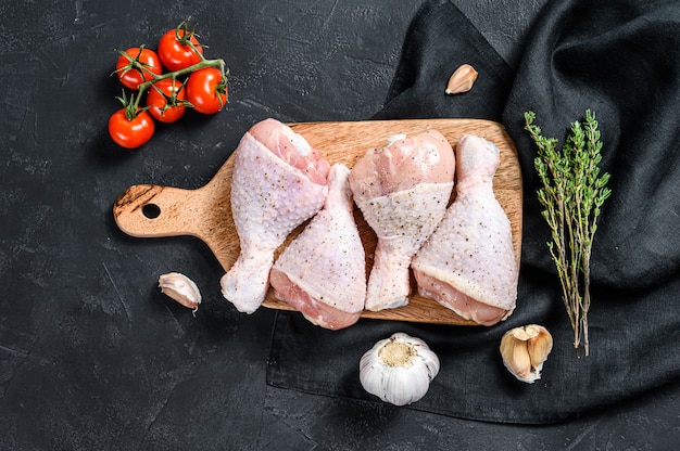 Cuisses de poulet crues aux épices et légumes sur une planche à découper en bois