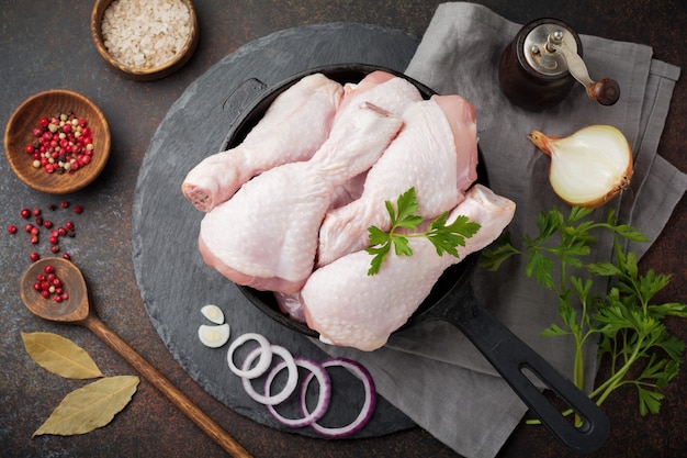 Cuisses de poulet crues sur une casserole en fonte avec des épices et des herbes sur un béton foncé ou une pierre préparée pour la cuisson.