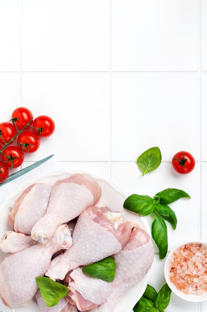 Cuisses de poulet crues avec, cerise tomate, herbes, basilic et épices, sur fond de marbre blanc, vue de dessus de l'espace de copie. Concept de déjeuner de régime alimentaire sain