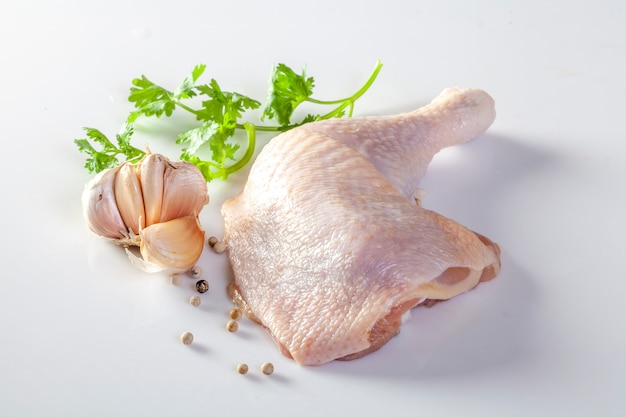 Cuisses de poulet crues avec des épices et des légumes sur un fond blanc