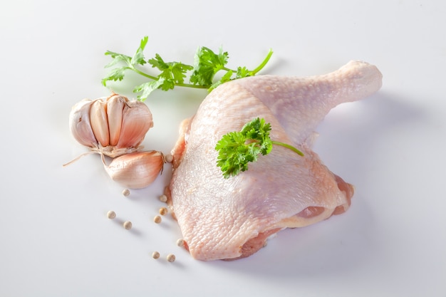 Cuisses de poulet crues avec des épices et des légumes sur un fond blanc