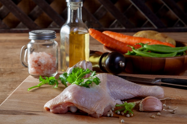 Cuisses de poulet crues avec des épices et des légumes sur une planche de bois