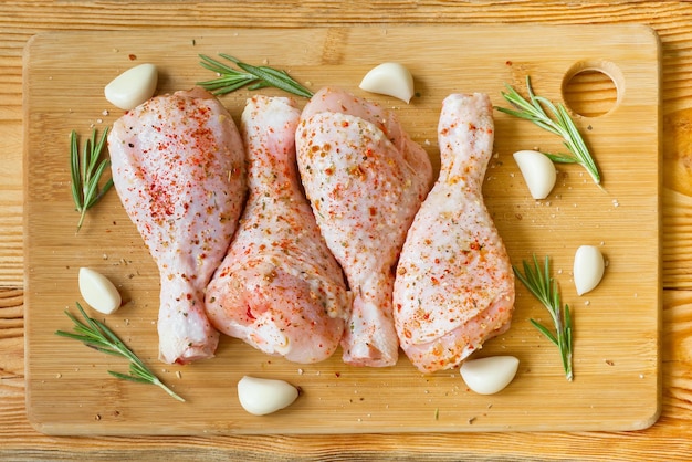 Cuisses de poulet crues marinées aux épices, ail et romarin sur une planche à découper en bois