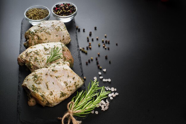 Cuisses de poulet crues marinées dans une sauce aux herbes sur fond sombre avec des épices fraîches au romarin