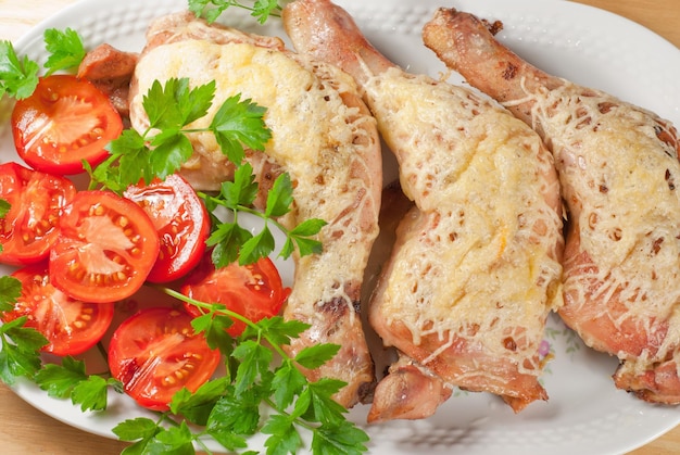 Cuisses de poulet frites avec du fromage et de la tomate servies sur la plaque blanche