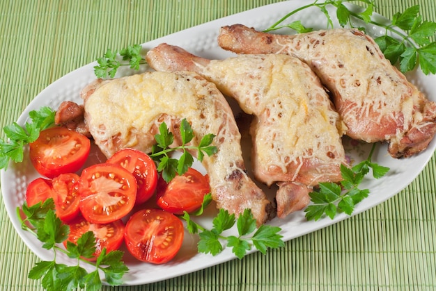 Cuisses de poulet frites avec du fromage et de la tomate servies sur la plaque blanche