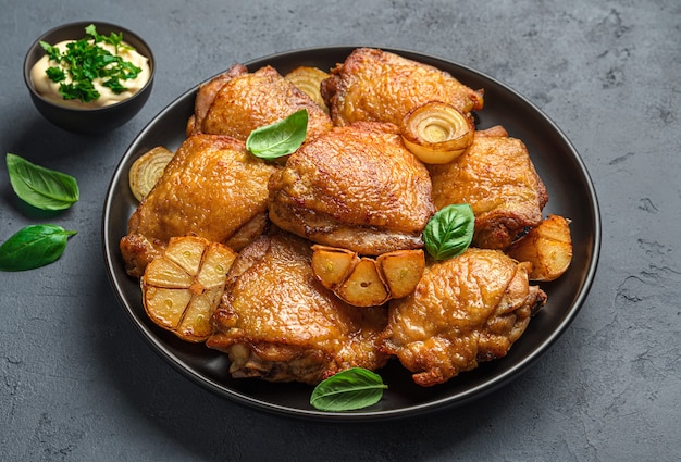 Cuisses de poulet frites avec oignon au basilic frais et sauce sur fond sombre Vue latérale en gros plan