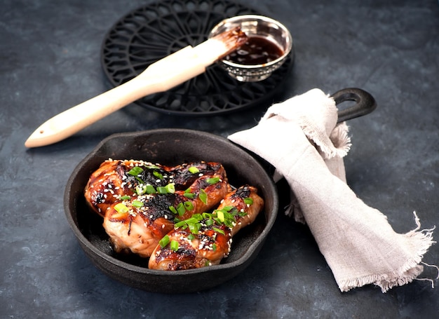 Cuisses de poulet frites avec sauce teriyaki et graines de sésame dans une poêle