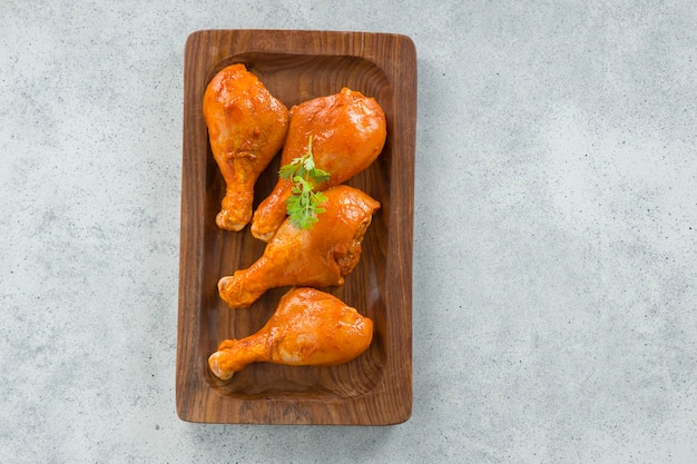 Cuisses de poulet marinées crues ou bâtonnets de tambour disposés dans une base en bois garnie de feuilles de coriandre fraîches qui sont placées sur un fond texturé blanc gris.