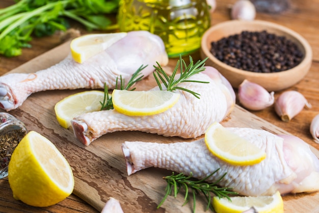 Cuisses de poulet non cuites crues, pilons sur planche de bois, viande avec ingrédients pour cuisiner