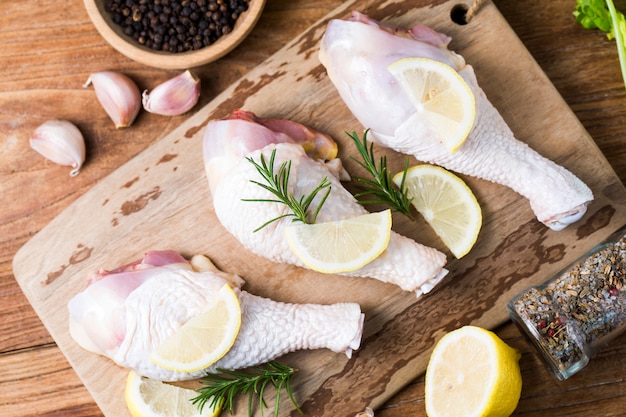 Cuisses de poulet non cuites crues, pilons sur planche de bois, viande avec ingrédients pour cuisiner