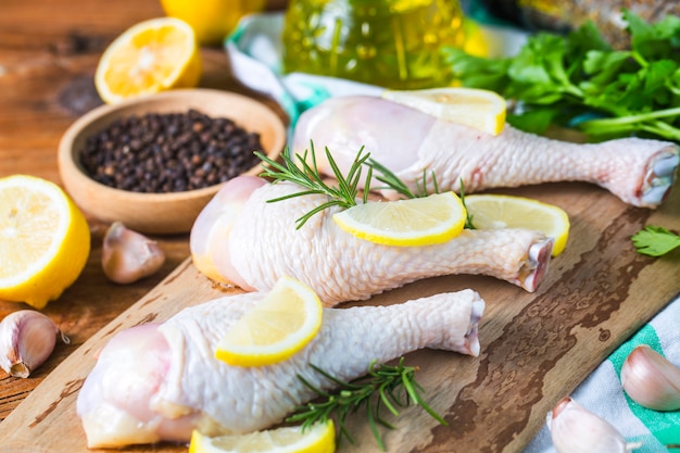 Cuisses de poulet non cuites crues, pilons sur planche de bois, viande avec ingrédients pour cuisiner